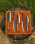 UA Knives Nile Forge chef knife set with five hand-forged carbon steel knives and a leather carry bag, displayed on a wooden surface.