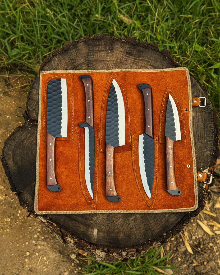 UA Knives Nile Forge chef knife set with five hand-forged carbon steel knives and a leather carry bag, displayed on a wooden surface.