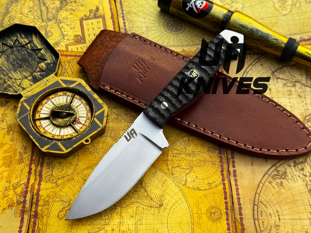 UA Knives Silver Myst camping hunting knife with hand-forged 12C27 steel blade and sheath, displayed on a wooden surface.